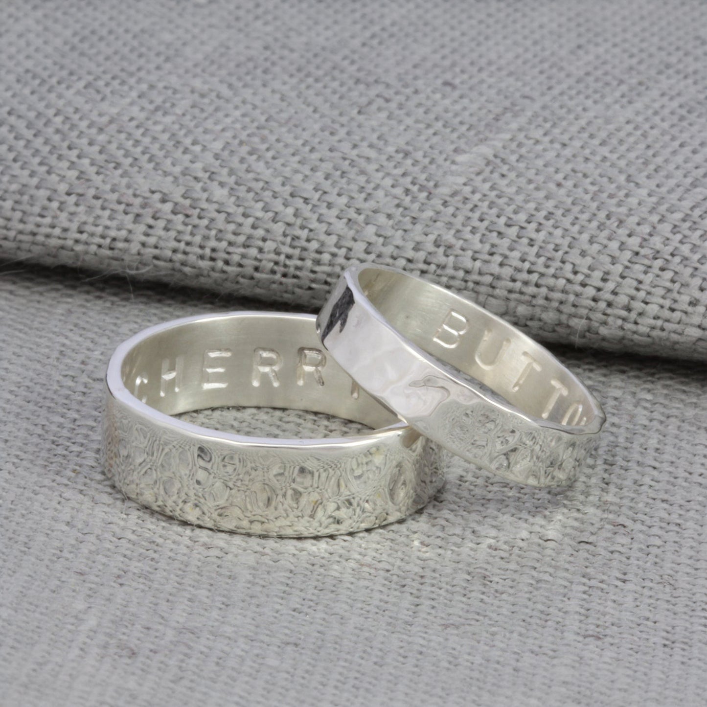 Close-up of personalised silver rings for couples with handstamped engraving on the inside band.