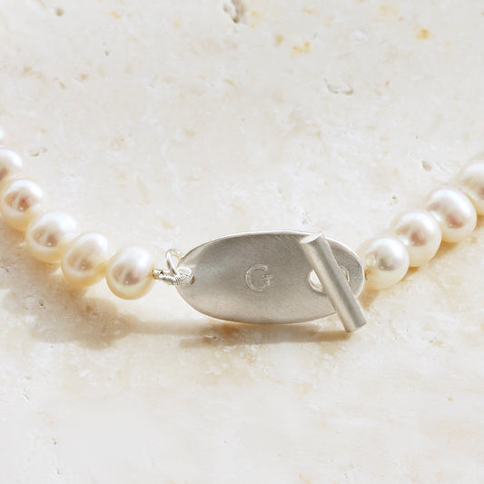 Close up of the oval charm with the initial 'G' handstamped in the middle, a T Bar style clasp connect this necklace at the front.