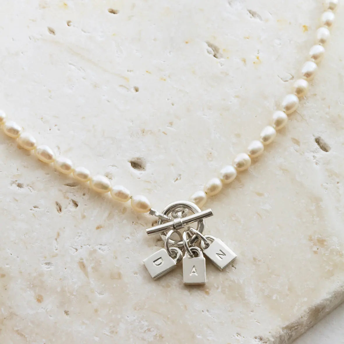 Close-up of freshwater pearl necklace with silver padlocks and t-bar clasp on a light background.