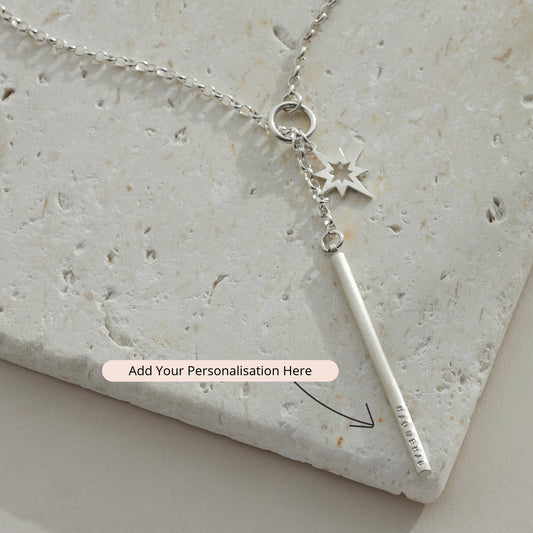 Flat lay of silver lariat necklace on stone background with celestial star detail and hand-stamped bar