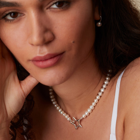 Model wearing white pearl necklace with silver star clasp, styled elegantly.