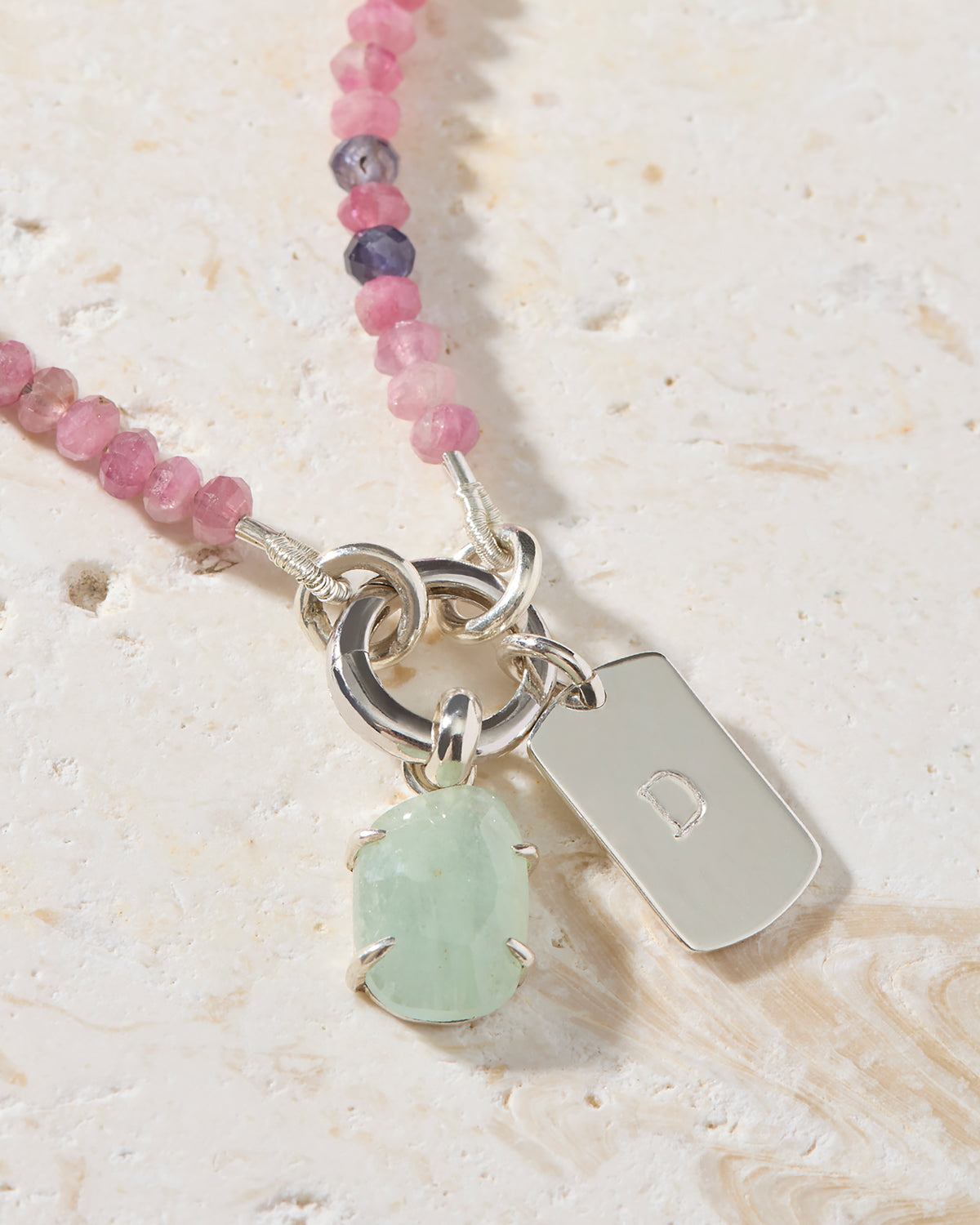 Close-up of hand-set aquamarine pendant and personalised sterling silver dog tag initial charm