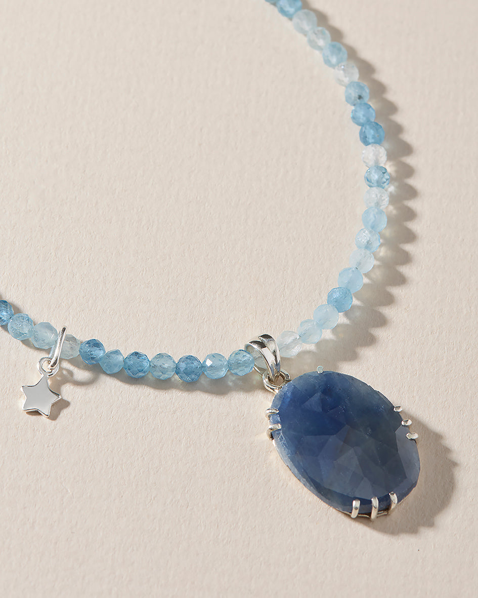 Close-up of hand-set blue sapphire pendant on a faceted aquamarine beaded necklace