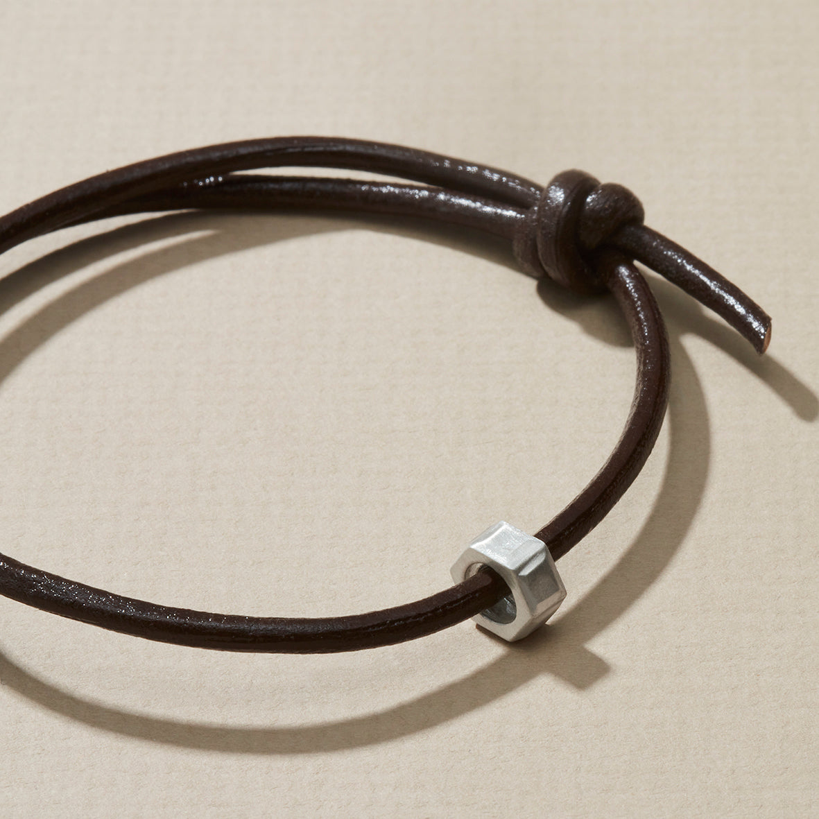 Close-up of personalised leather bracelet with silver hexagonal nut, dark brown leather cord.
