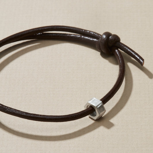 Close-up of personalised leather bracelet with silver hexagonal nut, dark brown leather cord.