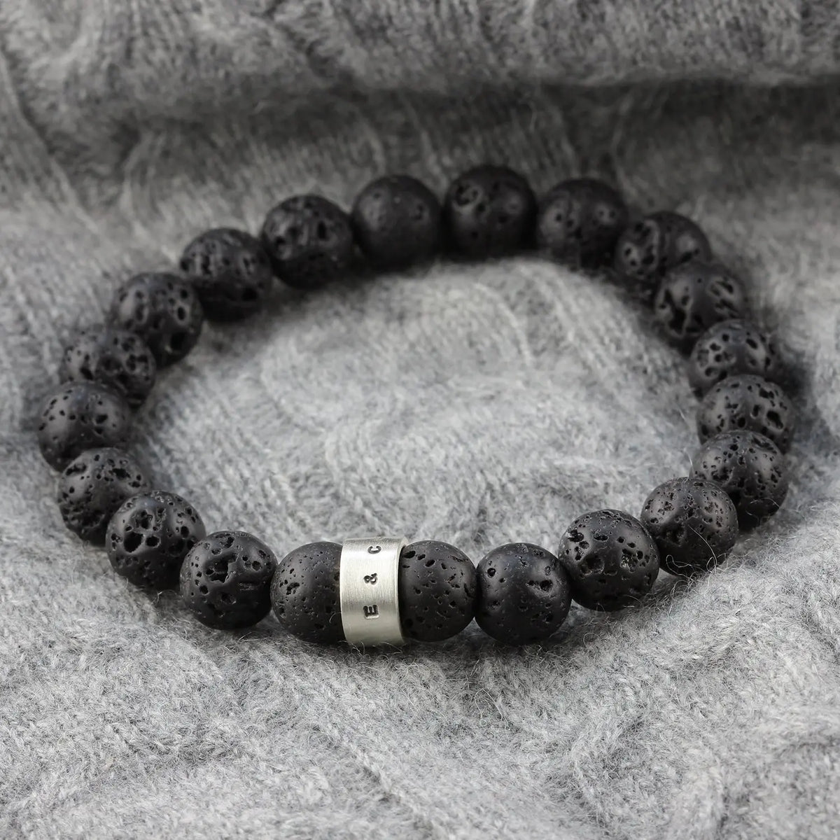 Men's black lava stone bead bracelet with naturally pitted volcanic beads and a personalised satin-finished sterling silver hoop, photographed on grey knitwear.
