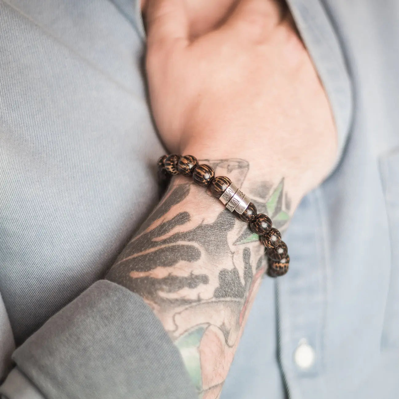 Close-up of hand-stamped sterling silver scroll on tiger ebony wood bead bracelet.