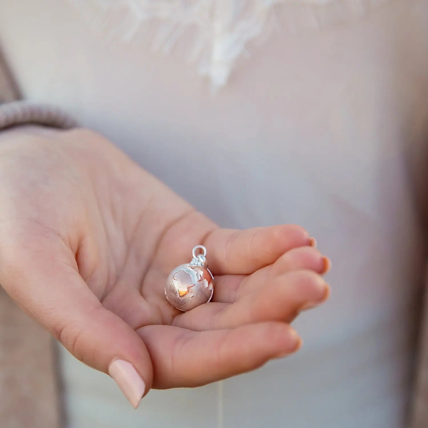 Personalised silver globe locket held in hand showing its textured world design
