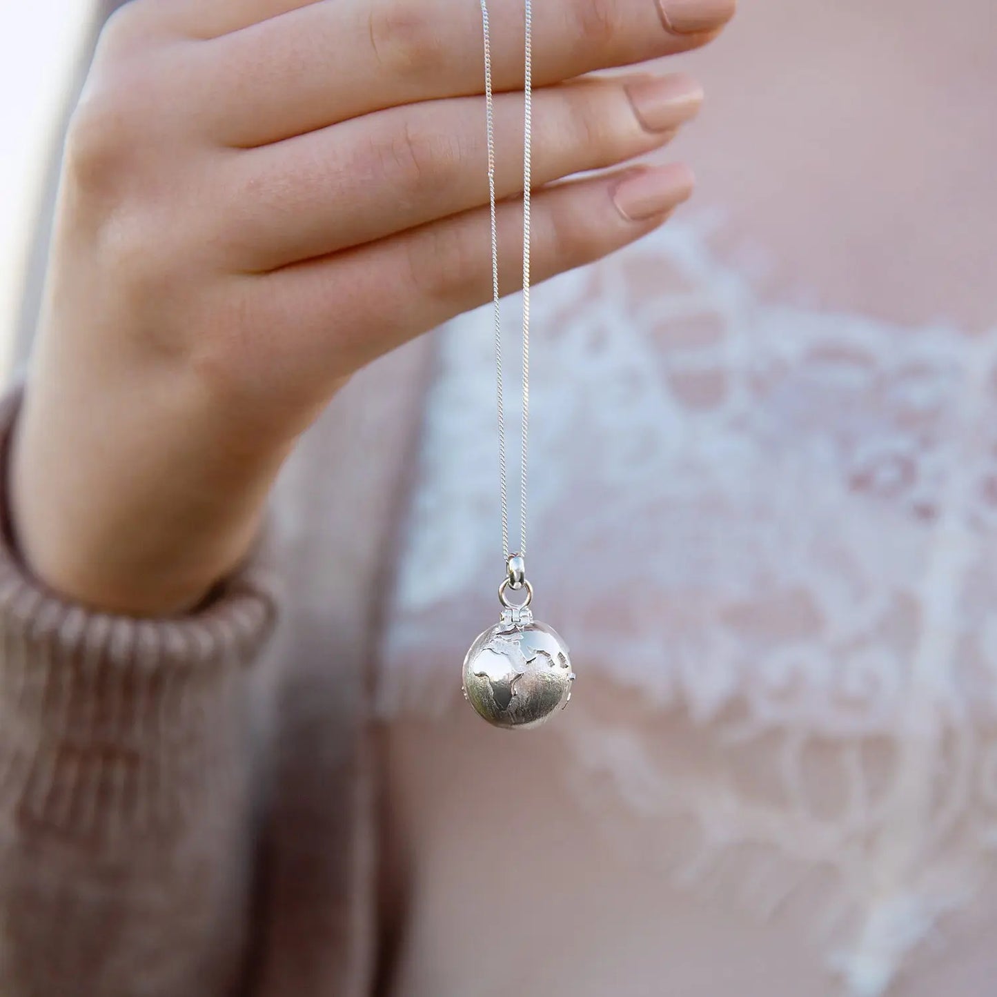 Sterling silver globe locket necklace held by its curb chain
