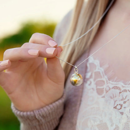 Silver globe locket necklace with yellow gold-plated continents worn close up
