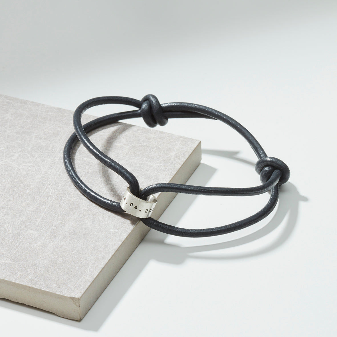 Dark leather bracelet with sterling silver story bead, perfect for personalisation, laid on a grey background.