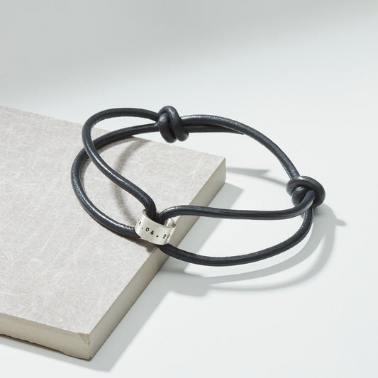 Dark leather bracelet with sterling silver story bead, perfect for personalisation, laid on a grey background.