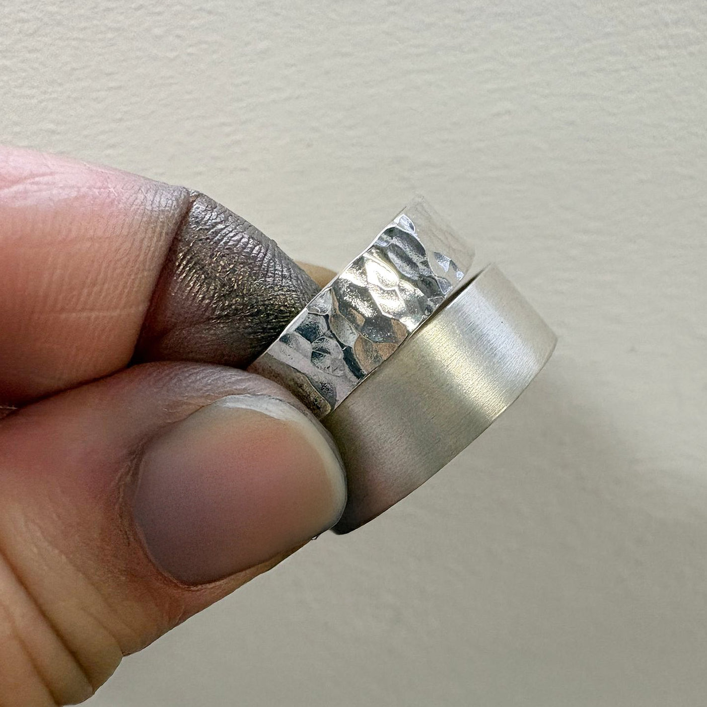 Silver ring held between fingers against a plain background