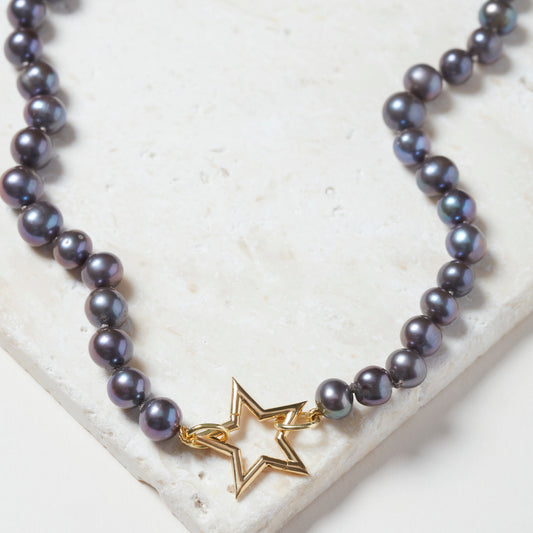 Close-up of peacock pearl necklace with sterling silver star clasp on a neutral background.
