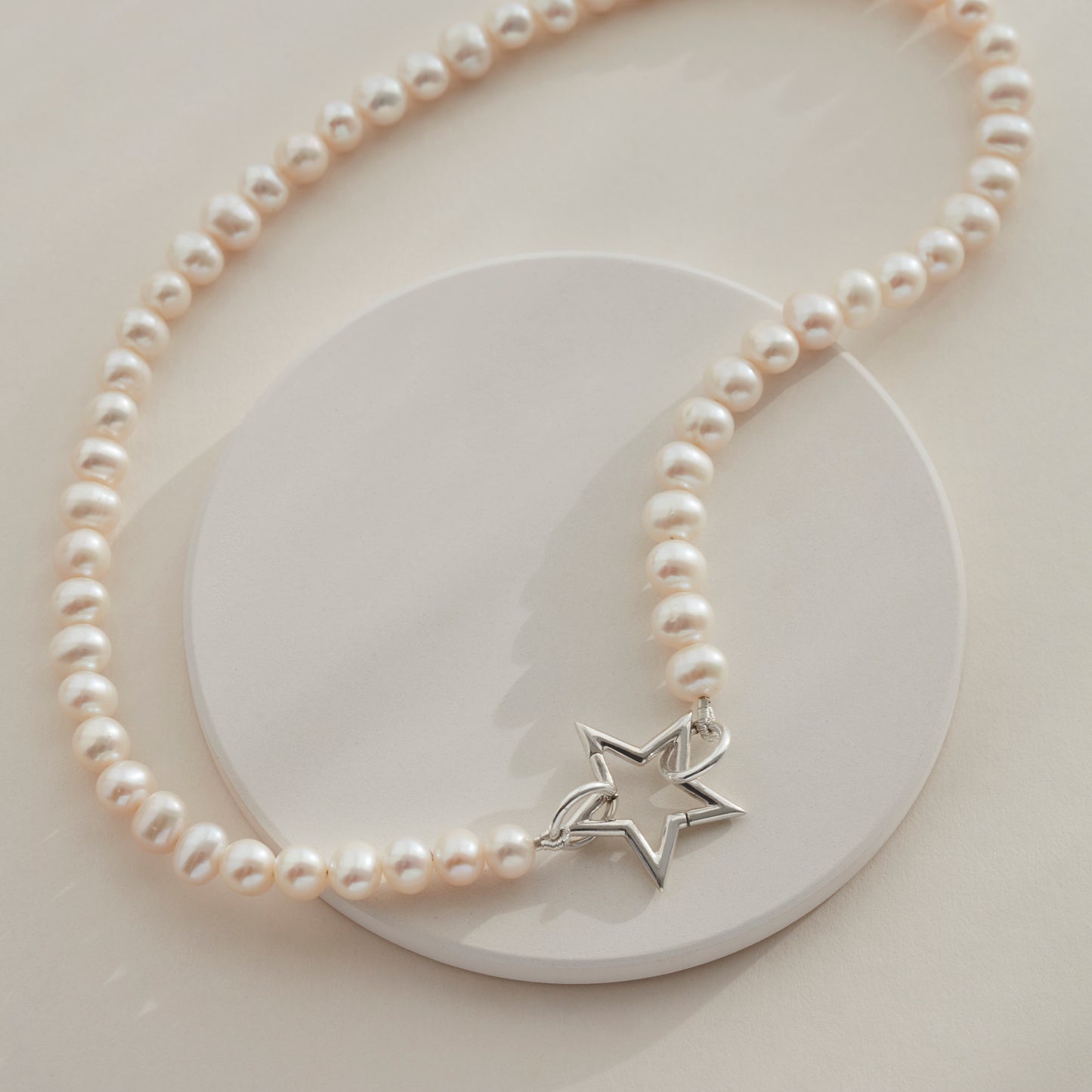 White freshwater pearl necklace with silver star clasp, draped on a circular plate.