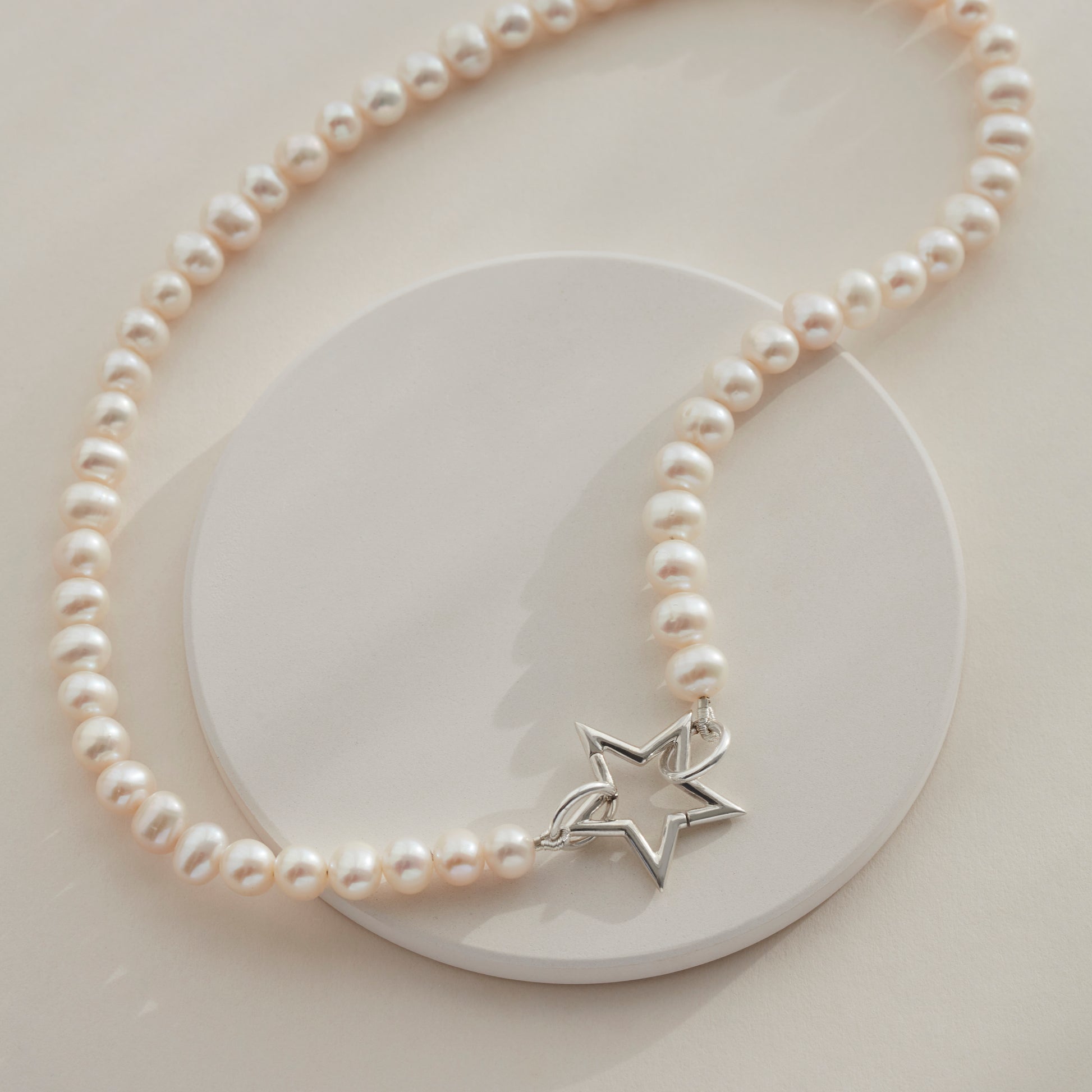 White freshwater pearl necklace with silver star clasp, draped on a circular plate.