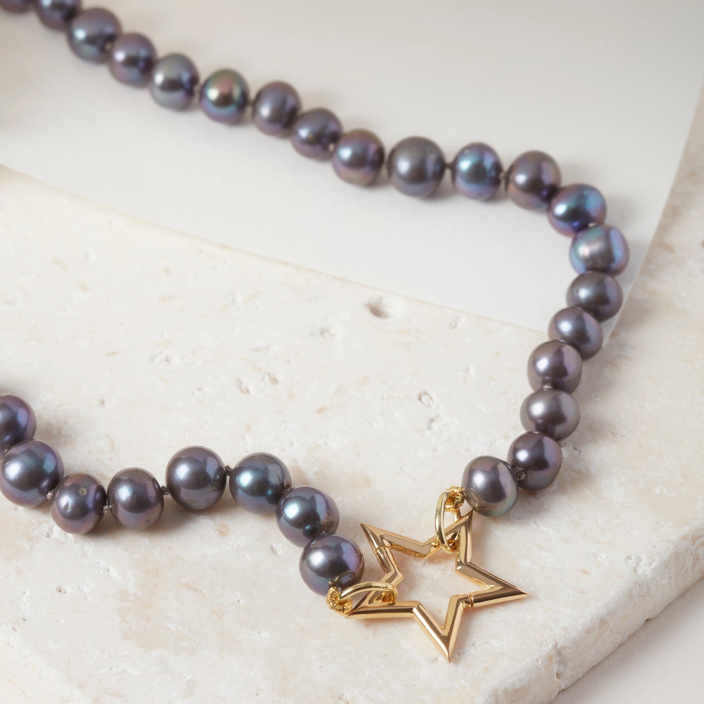 Peacock pearl necklace with 18ct gold vermeil star clasp, displayed on stone.
