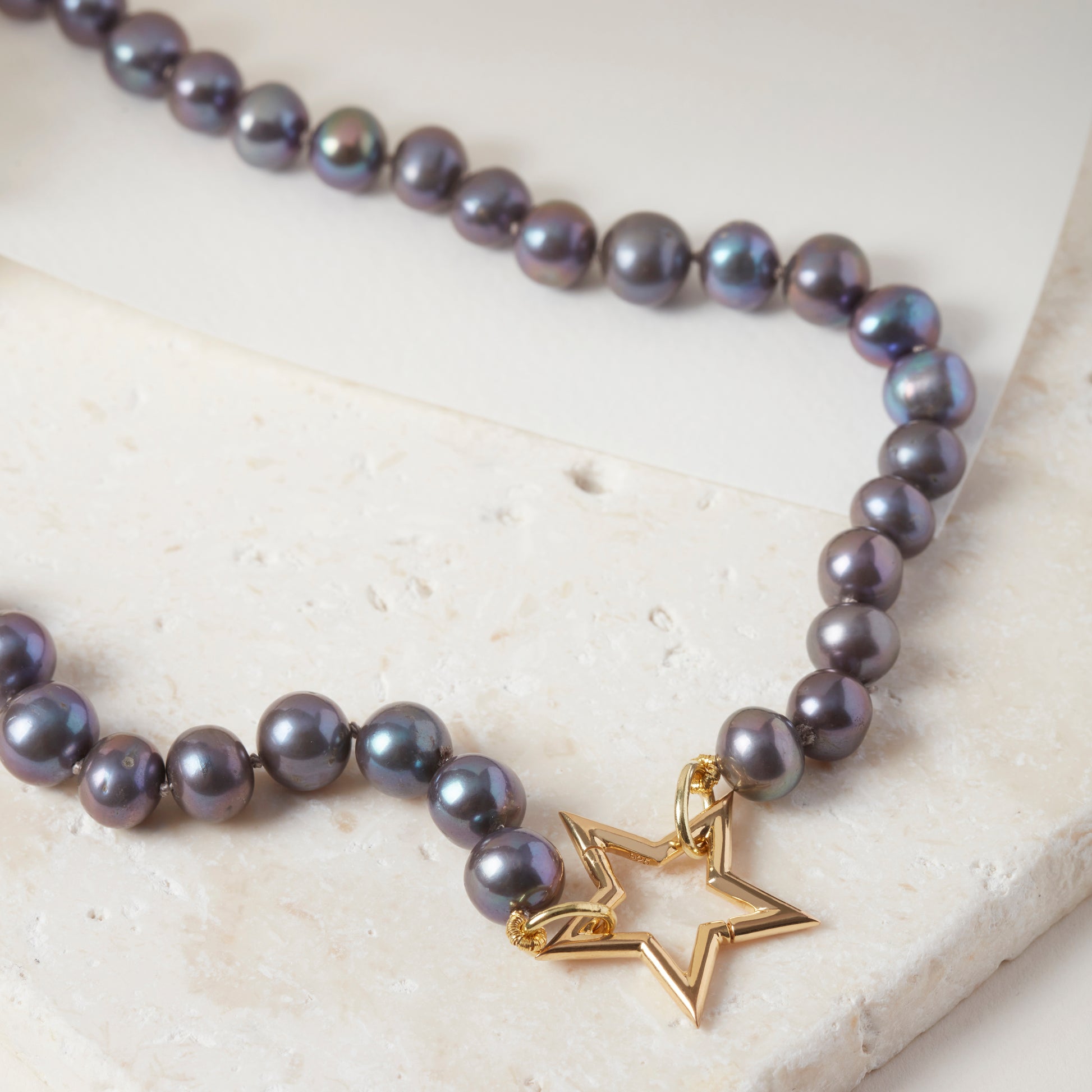Peacock pearl necklace with 18ct gold vermeil star clasp, displayed on stone.

