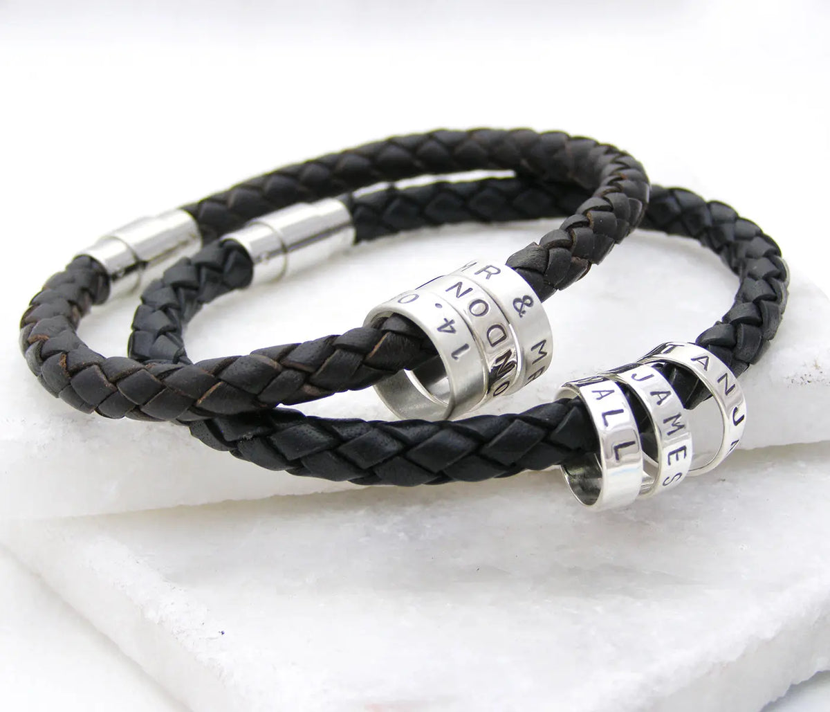 Two personalised men's braided leather bracelets with polished silver clasps and individually hand-stamped sterling silver hoops.