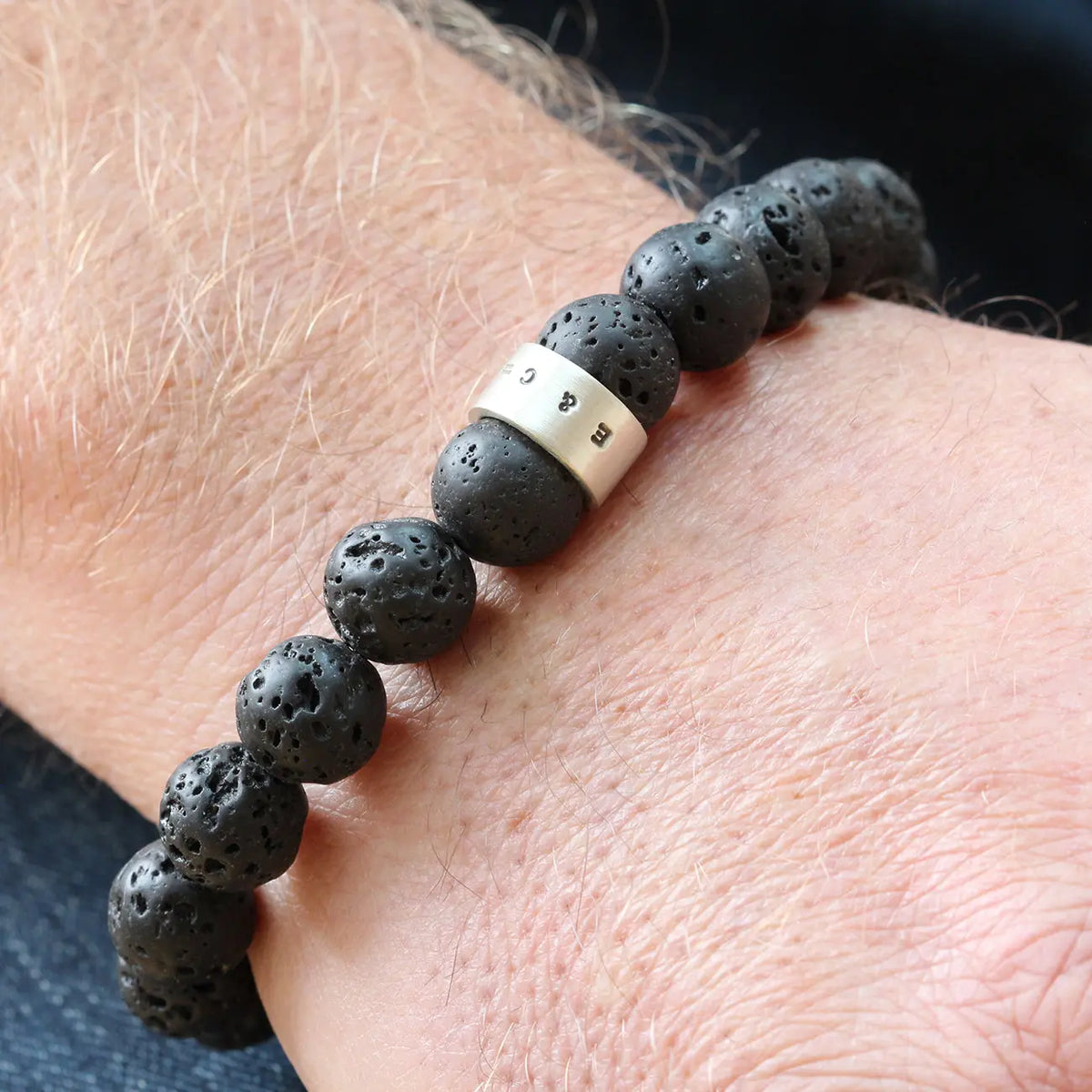Men's black lava stone bead bracelet worn on the wrist, featuring a personalised sterling silver hoop and rounded volcanic stone beads.