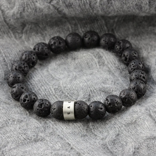 Men's black lava stone bead bracelet with naturally pitted volcanic beads and a personalised satin-finished sterling silver hoop, photographed on grey knitwear.